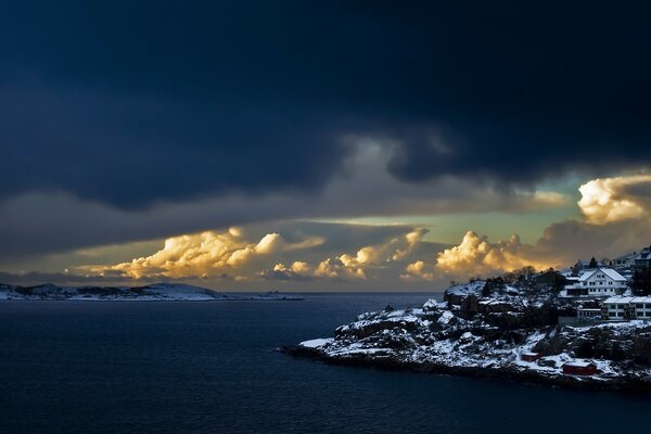 Maisons sur la côte enneigée sur fond de nuages énormes