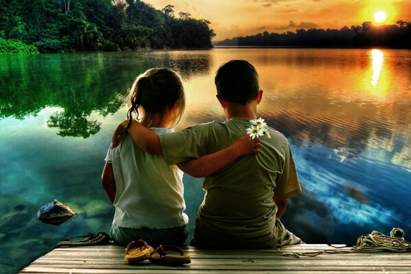Garçon et fille embrassés sur la rive de la rivière et regarder le coucher du soleil